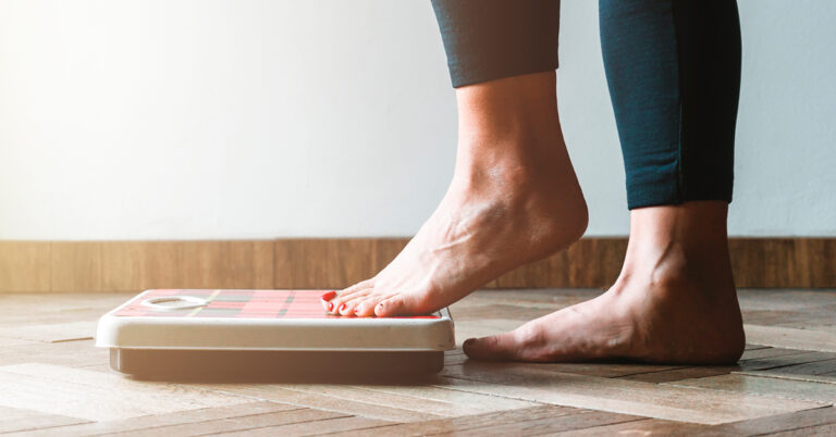 A woman steps on to a scale to weigh herself.