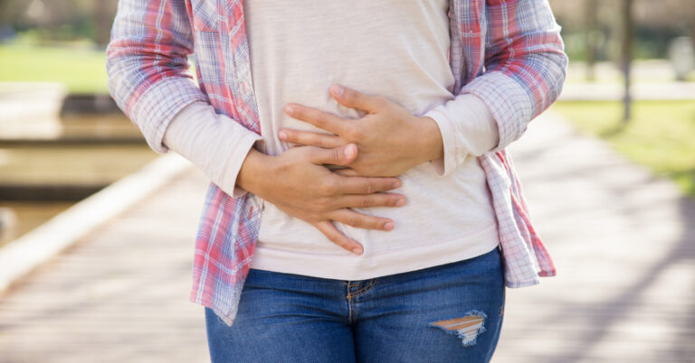 A woman hold her hands over her stomach, showing that she's experiencing stomach pain.
