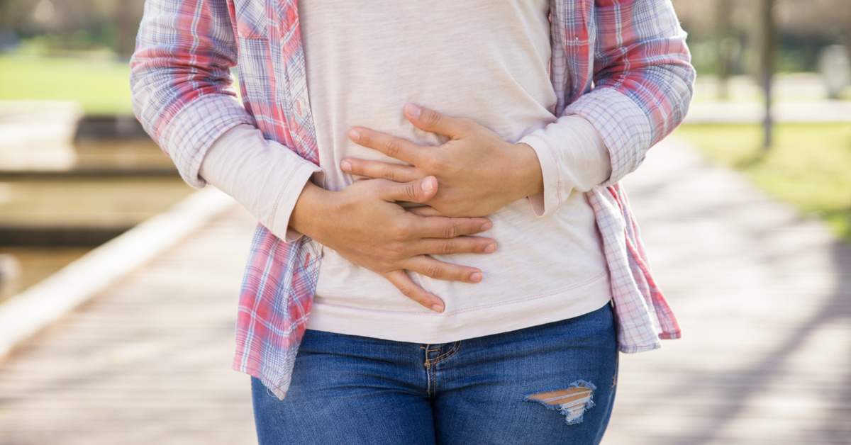 A woman hold her hands over her stomach, showing that she's experiencing stomach pain.