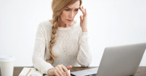 A middle aged woman looks at a laptop screen with confusion and concern.