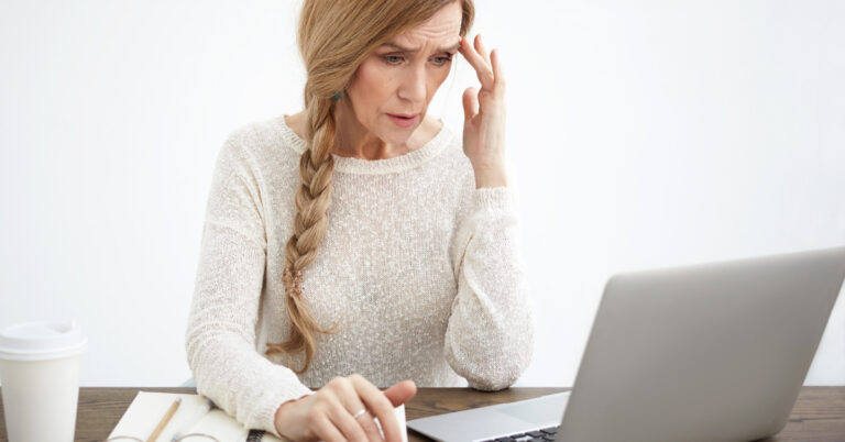 A middle aged woman looks at a laptop screen with confusion and concern.