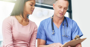 A woman speaks with a male doctor, reviewing test results.